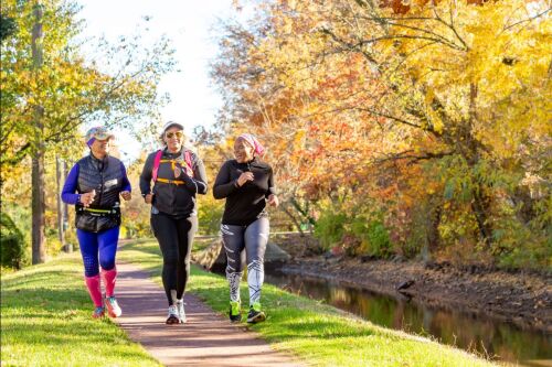 A group of three women jog on a trail beside autumn colors