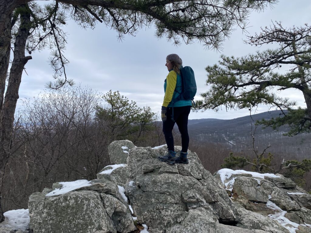 A woman stands on top of a mountain with a hiking backpack in the snow